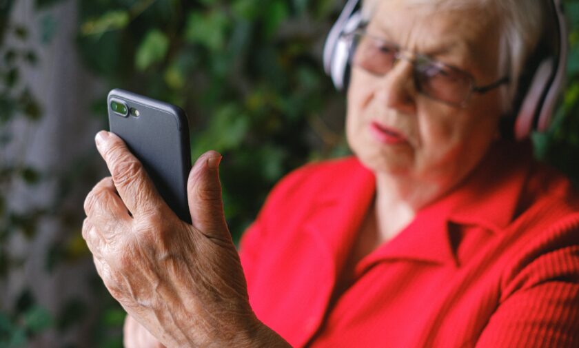 donna anziana con smartphone e cuffie alle orecchie